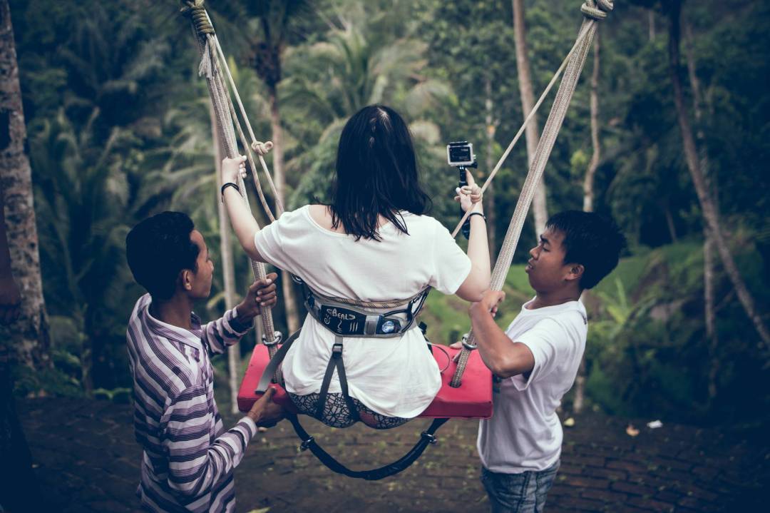 two men assisting woman riding on swing